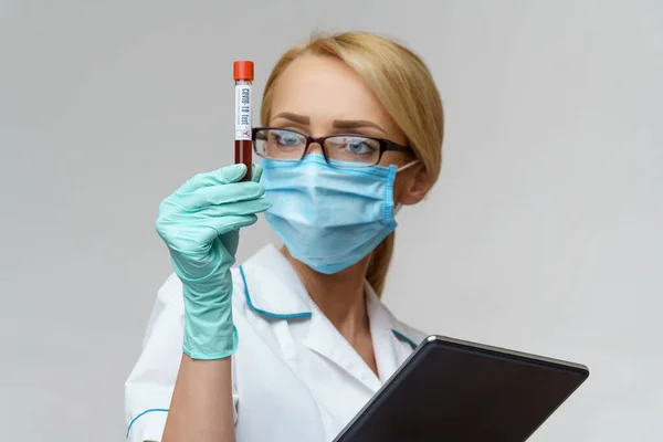 Médico enfermera mujer con máscara protectora y guantes - conteniendo el análisis de sangre del virus y tableta pc —  Fotos de Stock