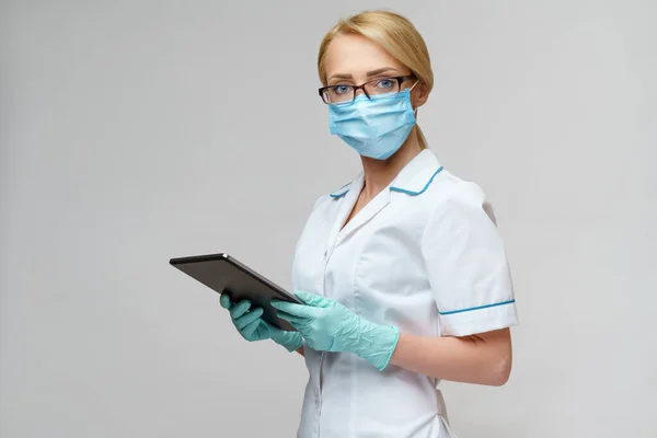 Médico médico enfermera mujer con máscara protectora y guantes - la celebración de la tableta de PC —  Fotos de Stock