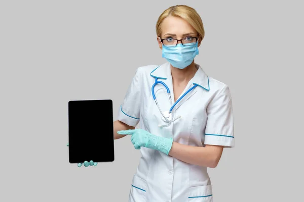 Médico médico enfermera mujer con máscara protectora y guantes - la celebración de la tableta de PC —  Fotos de Stock