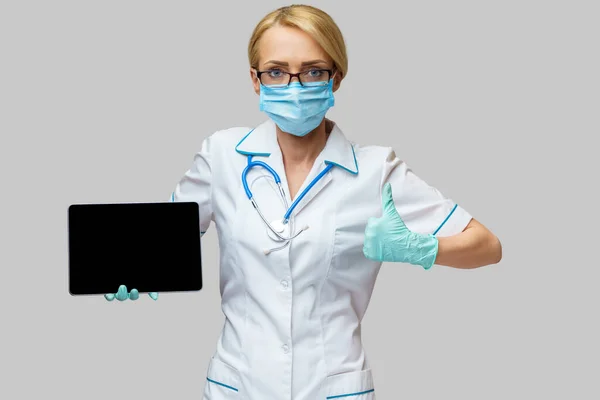 Médico médico enfermera mujer con máscara protectora y guantes - la celebración de la tableta de PC —  Fotos de Stock