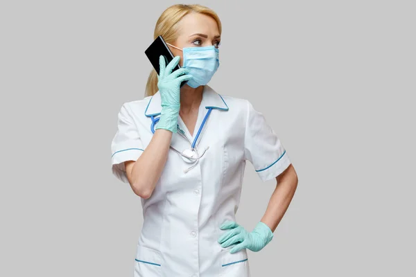 医療看護師の女性は保護マスクと手袋を着用 – 携帯電話を使用して — ストック写真