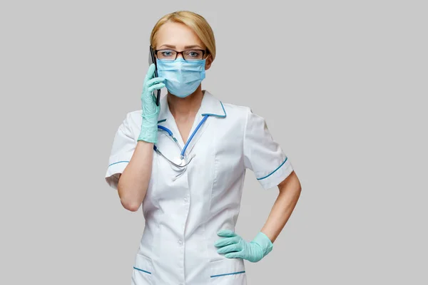 Medische arts verpleegkundige vrouw met beschermende masker en handschoenen - met behulp van mobiele telefoon — Stockfoto