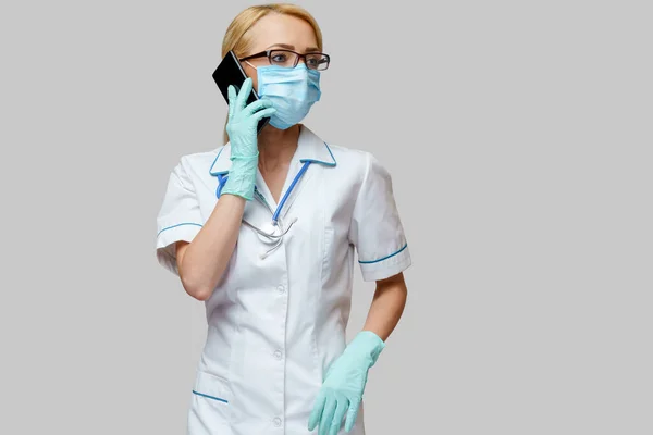 Medische arts verpleegkundige vrouw met beschermende masker en handschoenen - met behulp van mobiele telefoon — Stockfoto