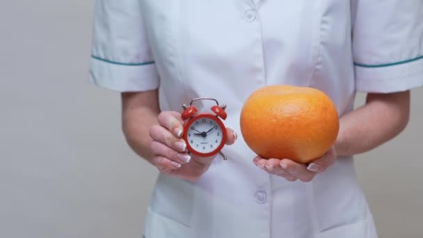 Nutritionist doctor healthy lifestyle concept - holding organic grapefruit fruit and alarm clock — Stock Video