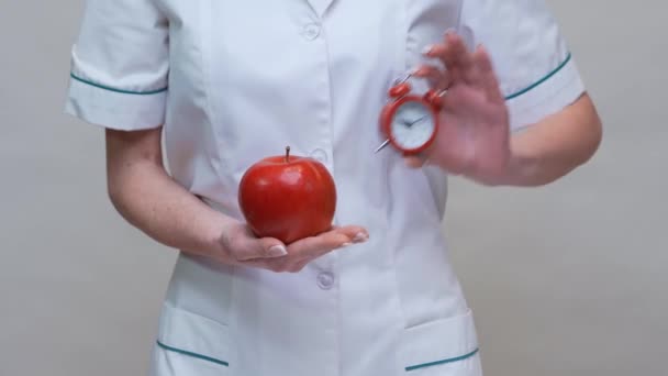 Nutritionist doctor healthy lifestyle concept - holding organic red apple and alarm clock — Stock Video