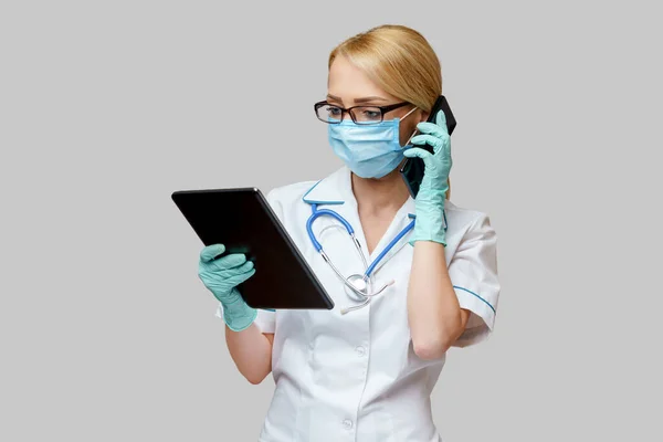 Verpleegkundige vrouw met beschermend masker en handschoenen - met tablet en mobiele telefoon — Stockfoto