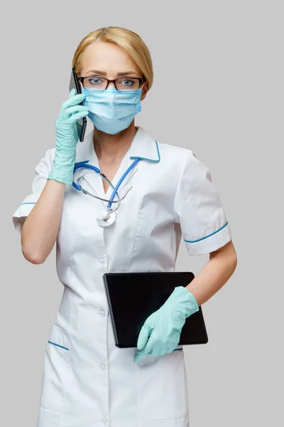 Médico enfermera mujer con máscara protectora y guantes - la celebración de la tableta PC y teléfono móvil — Foto de Stock