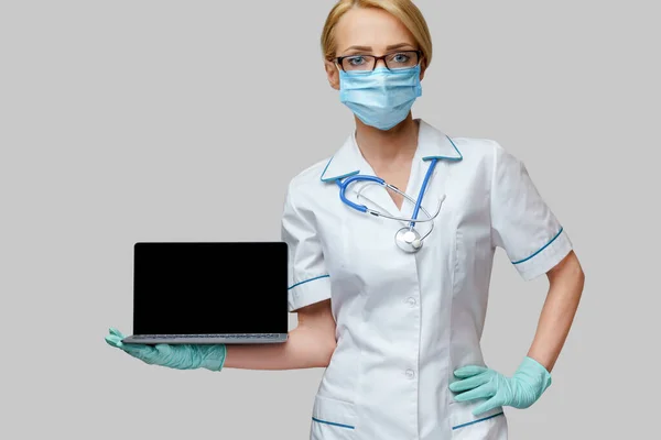 Koruyucu maske takan, eldiven takan, dizüstü bilgisayarı olan bir tıp doktoru. — Stok fotoğraf
