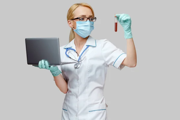 보호 마스크를 착용하고 장갑을 쥔 노트북 과 바이러스 혈액 검사 튜브를 착용하고 있는 의사 간호사 — 스톡 사진
