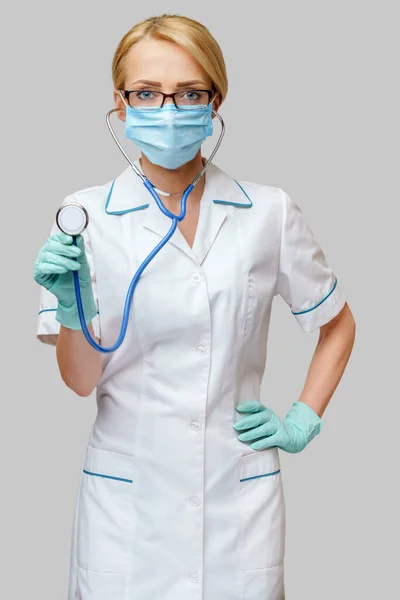보호용 마스크를 착용하고 밝은 회색 배경 위에 유액 장갑을 낀 청진기를 착용 한 여의사 — 스톡 사진
