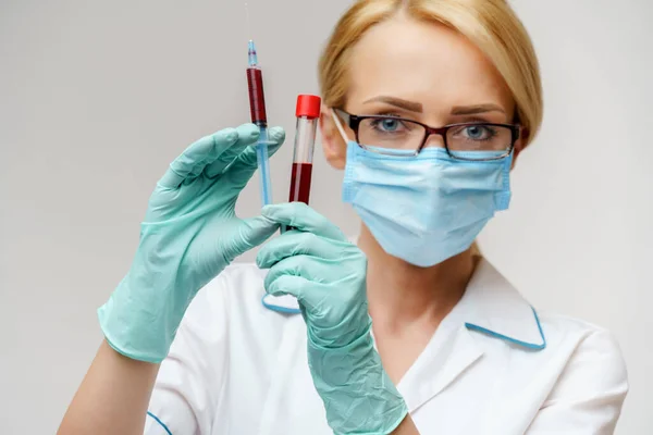 Doctor sau femeie asistentă medicală purtând mască de protecție care ține seringa și tubul de testare a sângelui — Fotografie, imagine de stoc