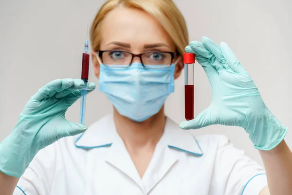 Doctor or woman nurse wearing protective mask holding syringe and blood test tube — Stock Photo, Image