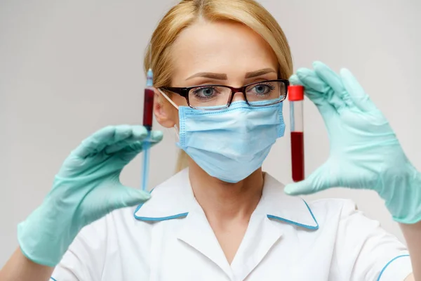 Dokter of verpleegkundige met een beschermend masker met spuit en bloedreageerbuis — Stockfoto