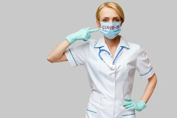 Femme médecin avec stéthoscope portant un masque protecteur et des gants en latex sur fond gris clair — Photo