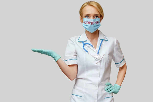 Doctora con estetoscopio con máscara protectora y guantes de látex sobre fondo gris claro — Foto de Stock