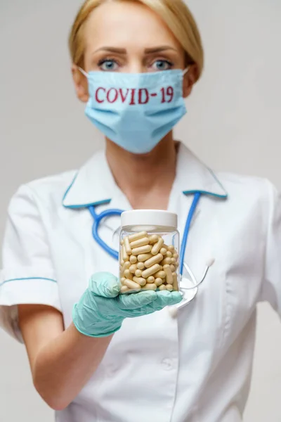 Medico infermiere donna con maschera protettiva e guanti di gomma o lattice - lattina contenente pillole — Foto Stock