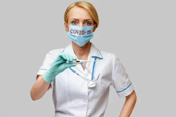 Врач медсестра женщина в защитной маске и резиновых или латексных перчатках - проведение термометра — стоковое фото
