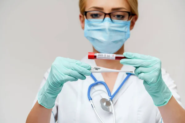 Médico enfermera mujer con máscara protectora y guantes - sosteniendo termómetro electrónico —  Fotos de Stock