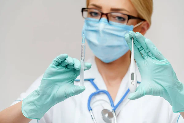Médico enfermera mujer con máscara protectora y guantes - sosteniendo termómetro electrónico y jeringa —  Fotos de Stock