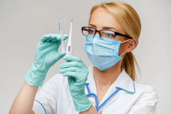 Ärztin Krankenschwester mit Schutzmaske und Handschuhen - mit elektronischem Thermometer und Spritze — Stockfoto