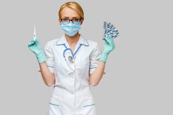 Enfermeira médica mulher usando máscara protetora e luvas de borracha ou látex - segurando bolhas de pílulas e termômetro — Fotografia de Stock