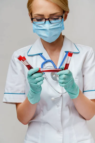 Médico enfermera mujer con máscara protectora y guantes - sosteniendo el tubo de análisis de sangre del virus —  Fotos de Stock
