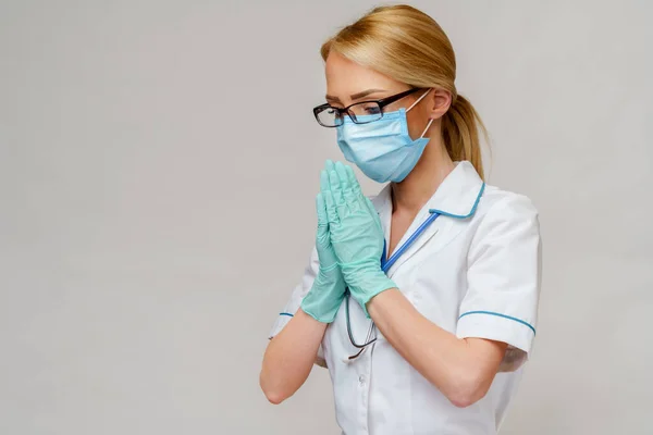 Lekarz pielęgniarka kobieta nosi maskę ochronną i rękawiczki lateksowe - modląc się nad nadzieją gest — Zdjęcie stockowe