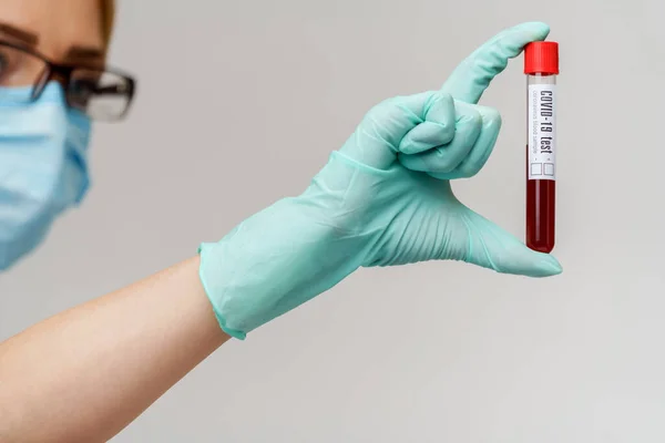 Mano en guante de látex sosteniendo la sangre en el tubo de ensayo de cerca — Foto de Stock