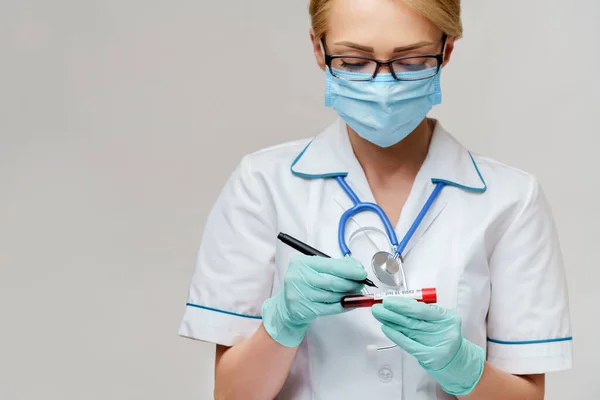 Lekarz pielęgniarka kobieta nosi maskę ochronną i rękawiczki - co znak po piórze na probówce badania krwi wirusa — Zdjęcie stockowe