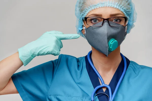 Vrouwelijke arts met stethoscoop dragen beschermende masker en latex handschoenen over lichtgrijze achtergrond — Stockfoto