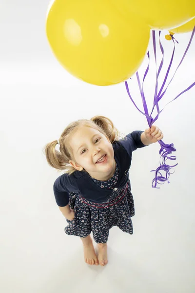 Retrato de una niña rubia sonriente sosteniendo globos amarillos — Foto de Stock