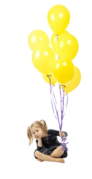 Niña aburrida sentada en el suelo sosteniendo globos de colores — Foto de Stock