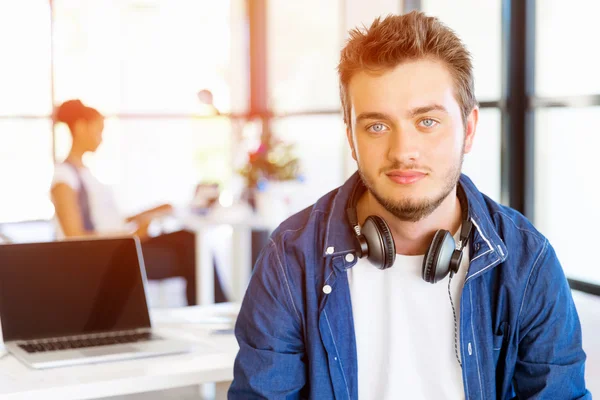 Junger Mann sitzt im Büro und schaut in die Kamera — Stockfoto