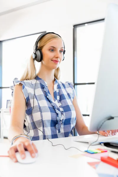 Молодая женщина слушает музыку во время работы за компьютером — стоковое фото