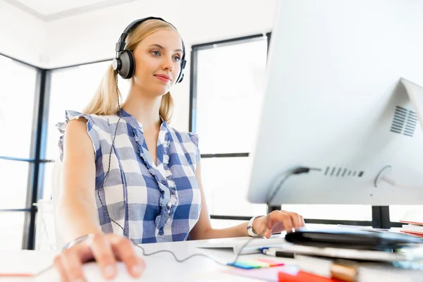 Mujer joven escuchando la música mientras trabaja en una computadora —  Fotos de Stock