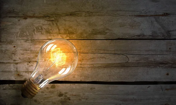 Light bulb on wooden surface . Mixed media — Stock Photo, Image