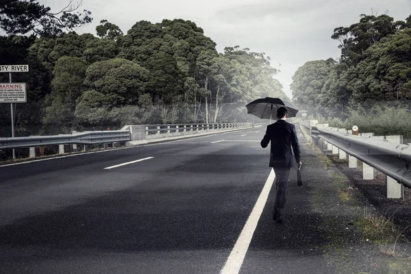 Vue arrière de l'homme d'affaires avec parapluie et valise marchant sur la route — Photo