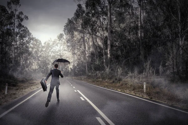 Οπίσθια όψη του επιχειρηματία με ομπρέλα και βαλίτσα περπατώντας στον δρόμο — Φωτογραφία Αρχείου