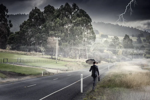 Οπίσθια όψη του επιχειρηματία με ομπρέλα και βαλίτσα περπατώντας στον δρόμο — Φωτογραφία Αρχείου