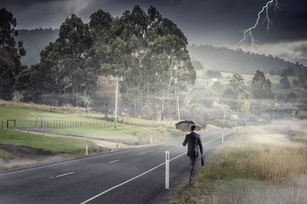 Vue arrière de l'homme d'affaires avec parapluie et valise marchant sur la route — Photo