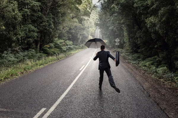 Rückansicht des Geschäftsmannes mit Regenschirm und Koffer, der auf der Straße läuft — Stockfoto