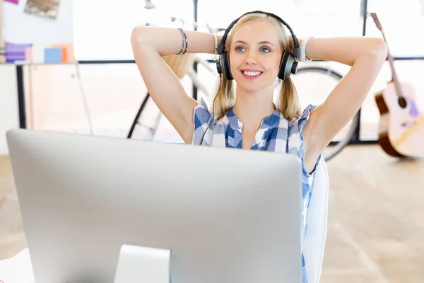 Mujer joven escuchando la música mientras trabaja en una computadora — Foto de Stock