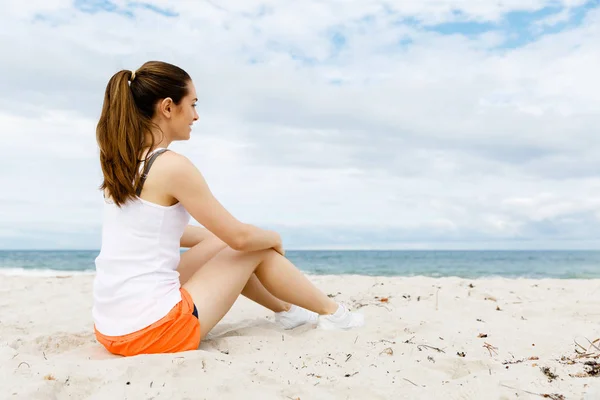 Młoda kobieta w sportowych nosić siedzi na plaży — Zdjęcie stockowe