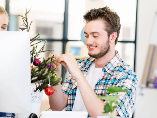 Молодий чоловік прикрашає ялинку в офісі — стокове фото