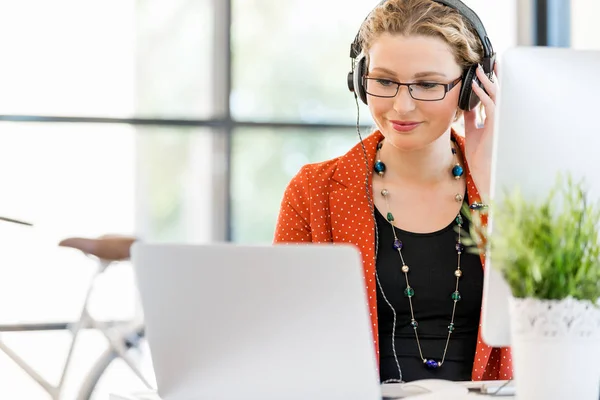 Junge Frau hört Musik, während sie am Computer arbeitet — Stockfoto