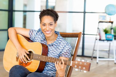 Gitar ile iş içinde oturan Afro-Amerikan ofis çalışanı gülümseyen portresi