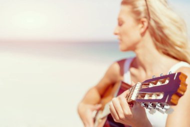 Güzel genç bir kadın sahilde gitar çalıyor.