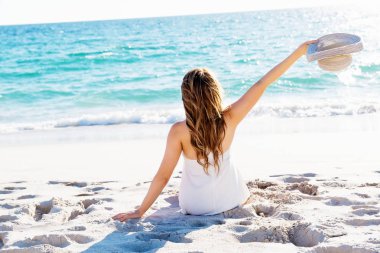 Genç bir kadın sahilde oturuyor.