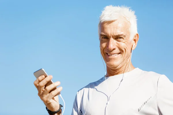 Male runner with his mobile smart phone standing outdoors — Stock Photo, Image