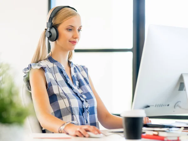 Junge Frau arbeitet im Büro mit Kopfhörern — Stockfoto